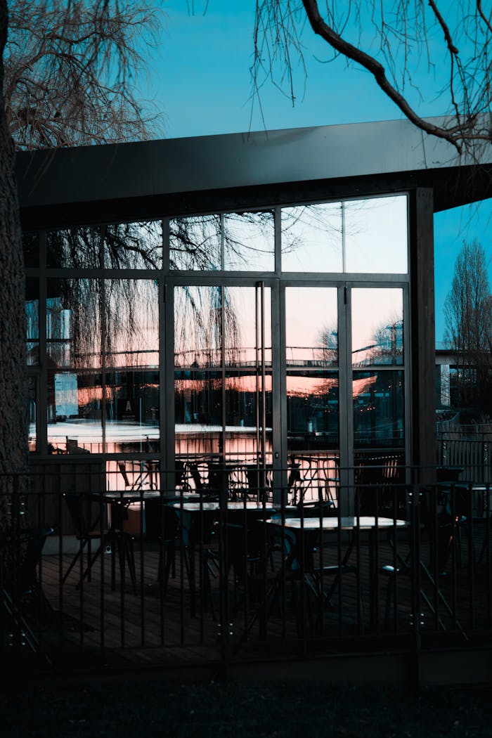 A modern building with glass windows reflecting the sunset view, featuring empty outdoor seating.