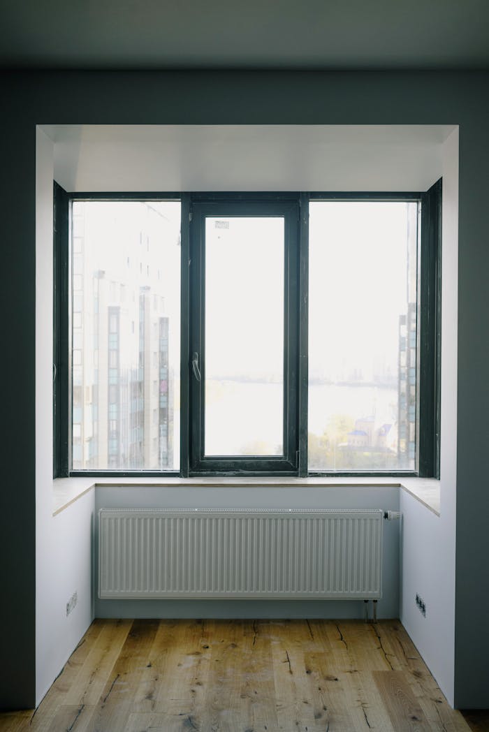 Wide transparent rectangular window and simple radiator in enclosed balcony with furniture in daytime