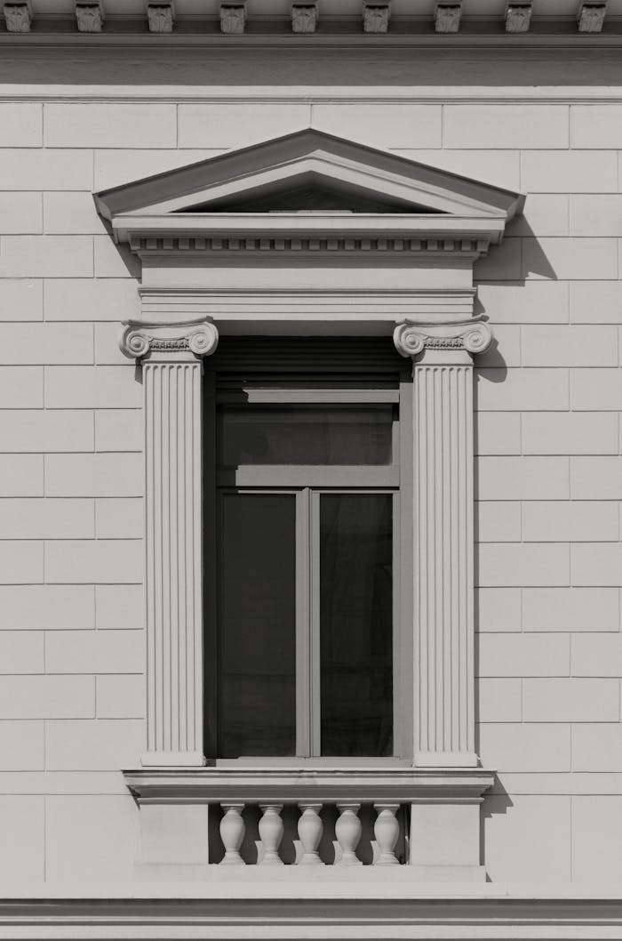 Detailed black and white photo of a classic window with columns and pediment.