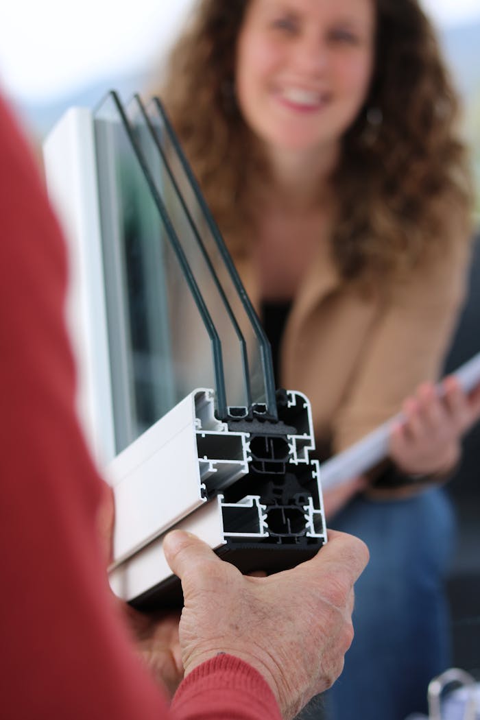 Close-up of hands holding a double-glazed window pane with a woman smiling in the background.